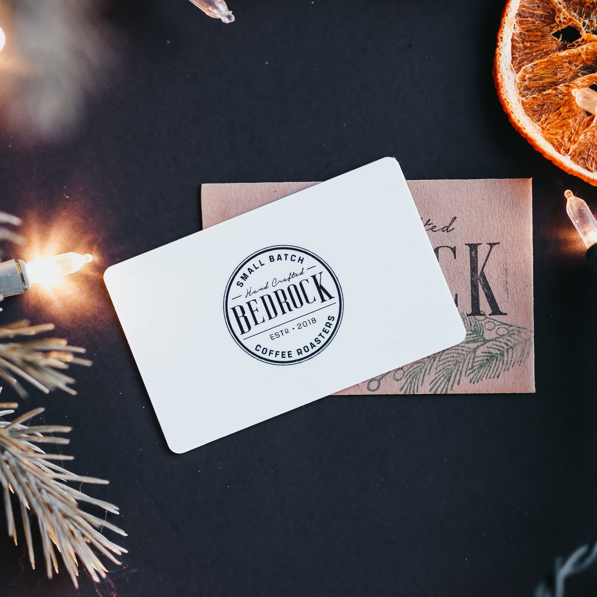 Gift card with a brand logo on a dark surface with Christmas decorations.